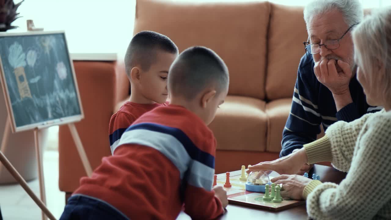 双胞胎小男孩和祖父母一起玩棋盘游戏，家庭娱乐，儿童社交活动视频素材