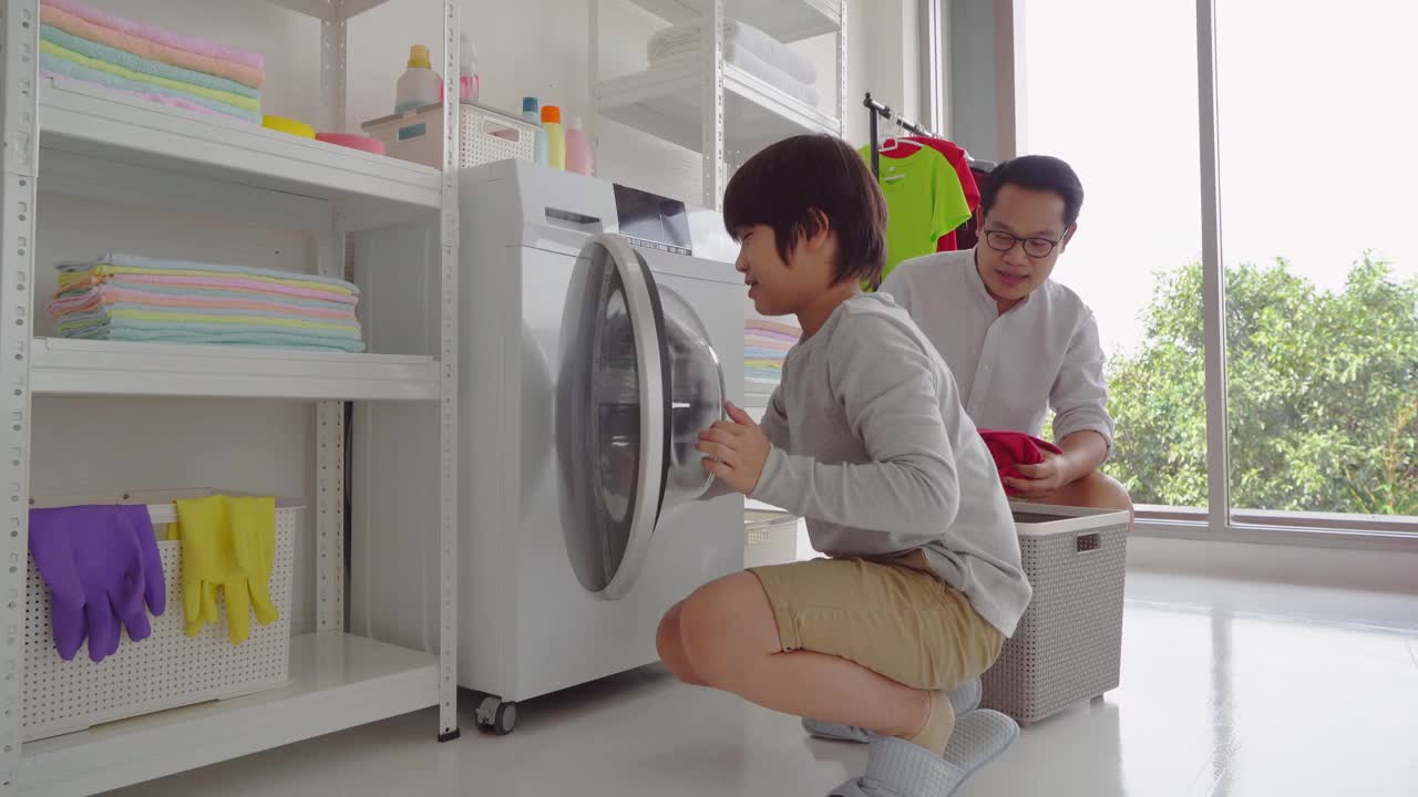 亚洲父亲和他的儿子在洗衣机在家里一起洗衣服的家庭家务团聚的概念。视频素材