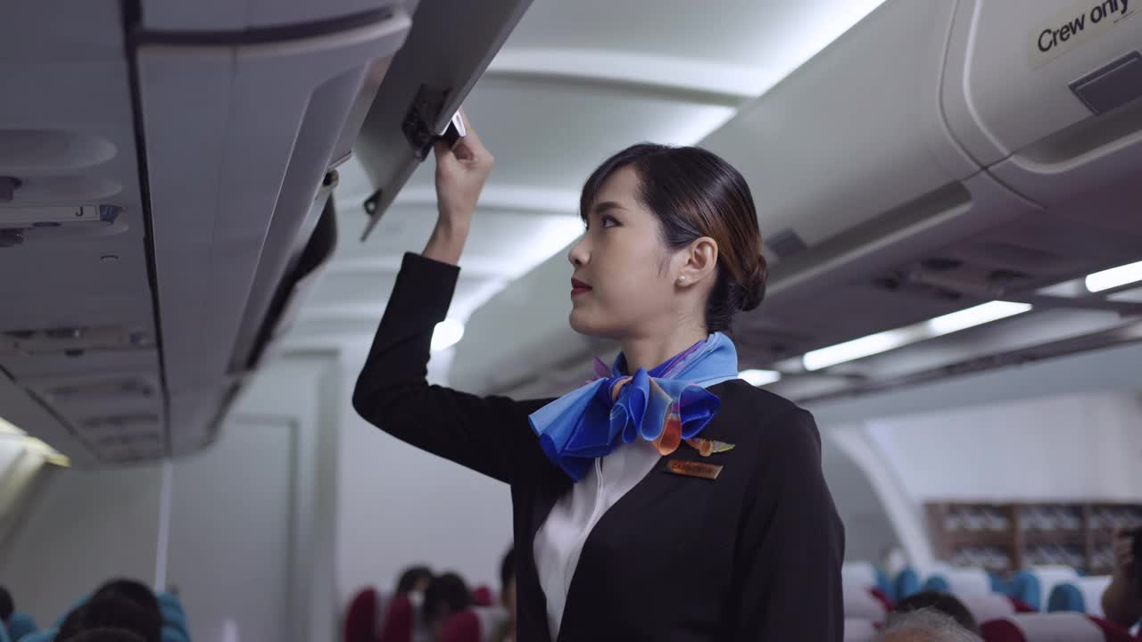 在一架飞机上，一名女乘务员关闭头顶上的储物柜视频素材