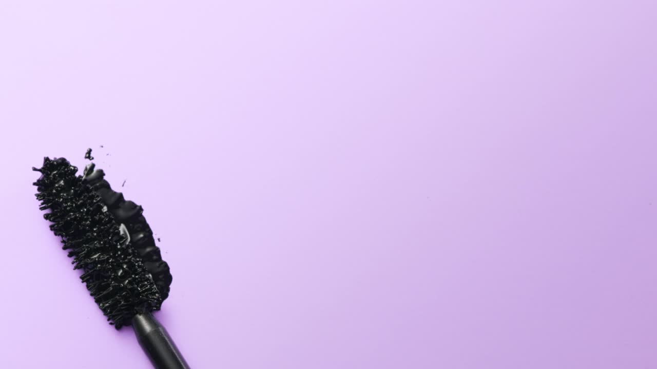 近距离和慢动作的黑色睫毛膏创造了一个睫毛膏棒在紫色的背景视频素材