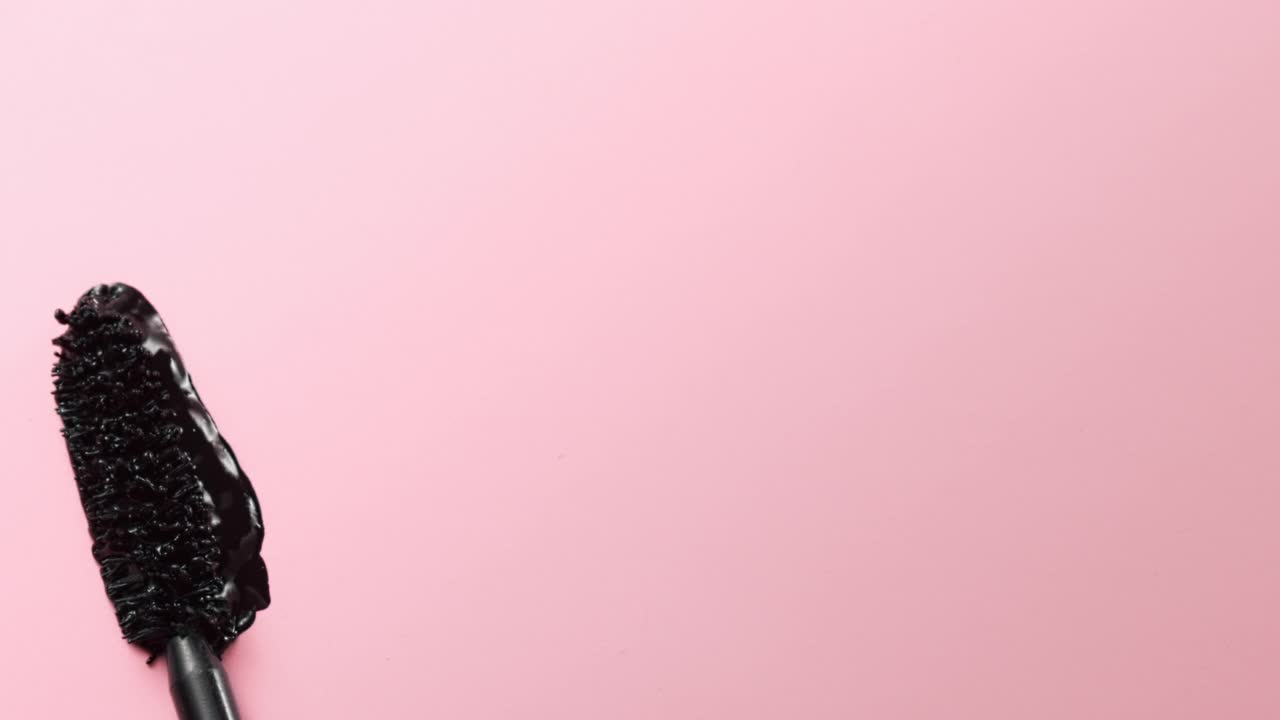 近距离和慢动作的黑色睫毛膏创造了一根睫毛棒在浅粉色的背景视频素材