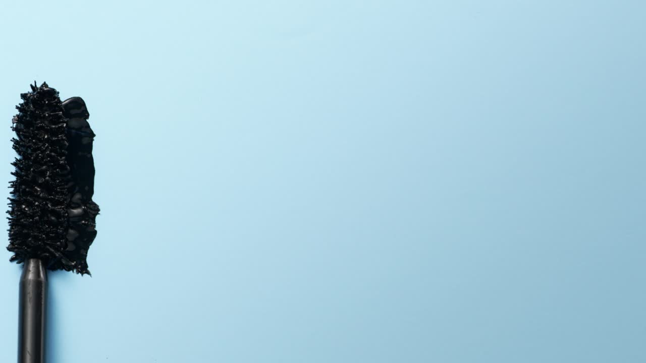 近距离和慢动作的黑色睫毛膏创造了一根睫毛棒在浅蓝色的背景视频下载