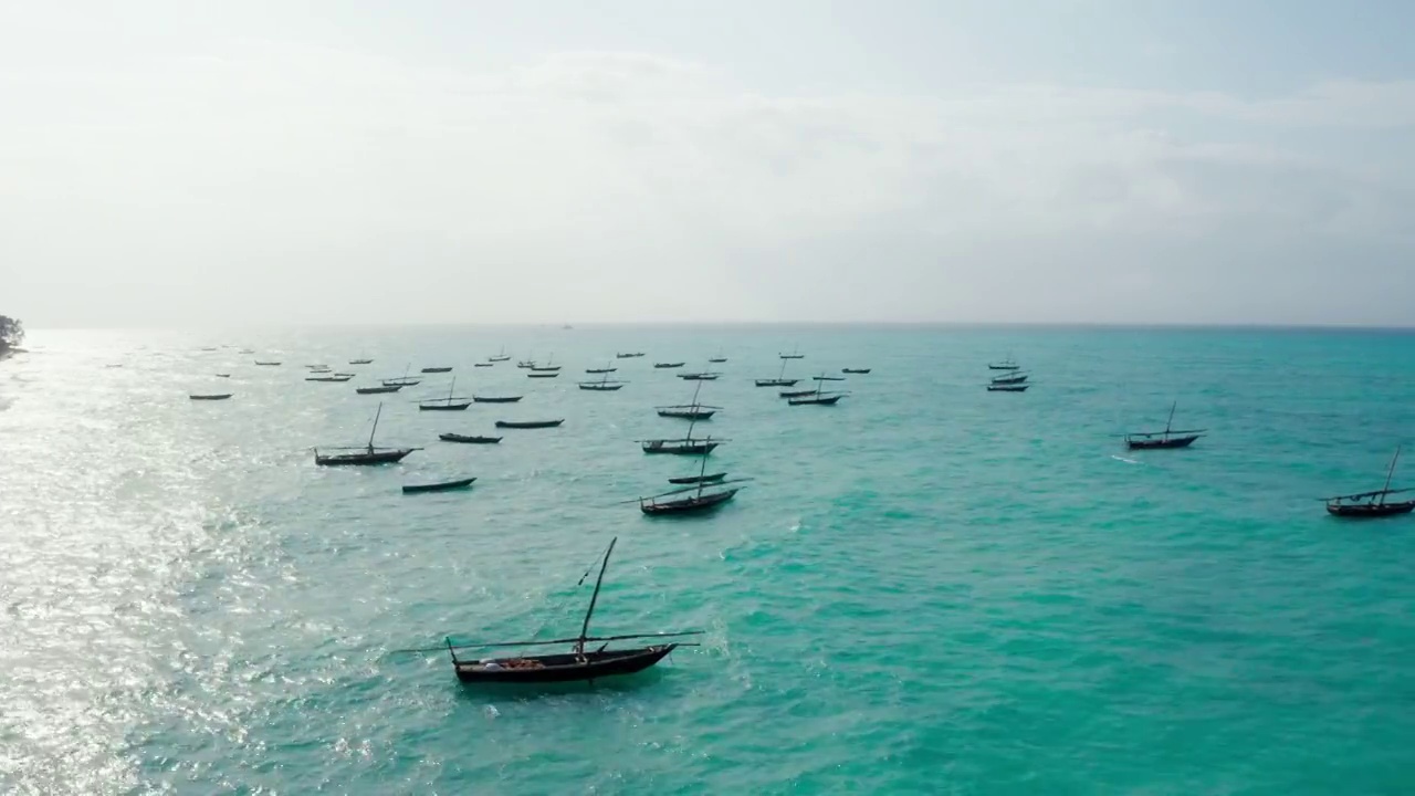 航拍渔船漂浮在碧绿的印度洋波浪附近的桑给巴尔岛，坦桑尼亚。无人机点俯视图4K视频。旅游和渔业概念视频。视频下载