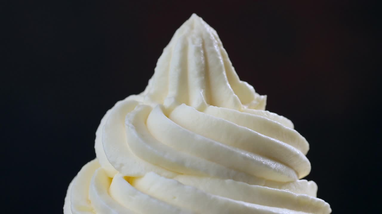 融化的焦糖酱在旋转的奶油上流动，接近黑色的背景视频下载