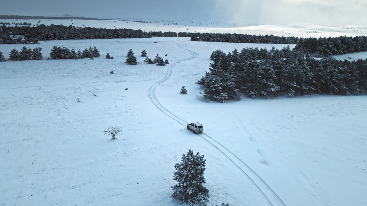 空中拍摄的白色汽车在被雪覆盖的道路上行驶视频下载
