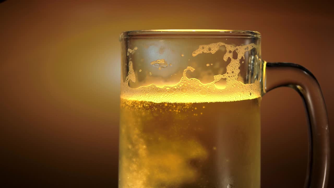 将啤酒倒入一个透明的杯子，啤酒泡沫和泡沫视频素材