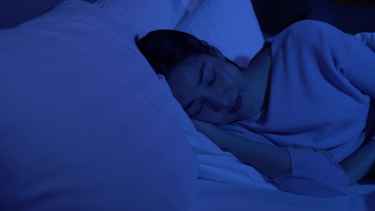 安静漂亮的年轻女人晚上闭着眼睛睡在她舒适的床上，盖着毯子。视频下载