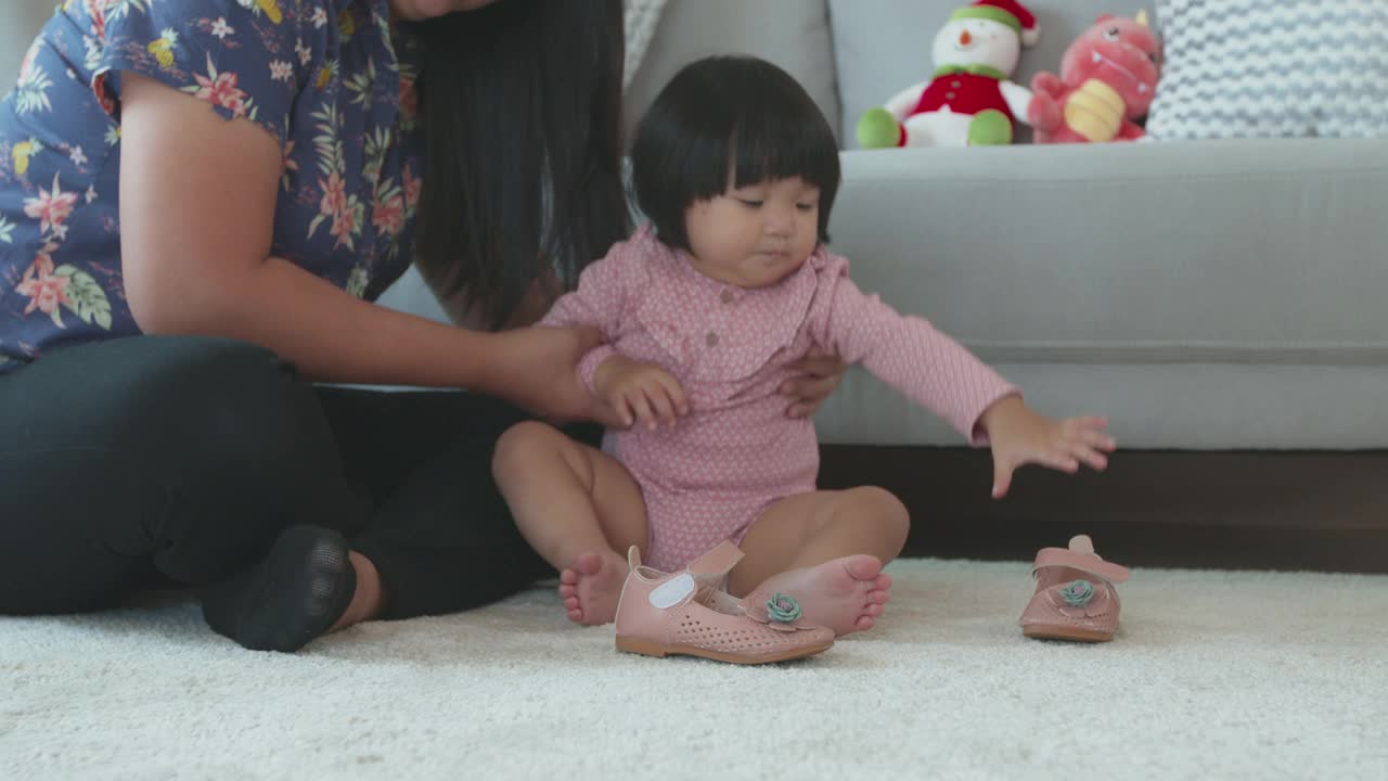 妈妈帮她的可爱的亚洲蹒跚学步的小女孩穿鞋之前一起出去。童年与家庭生活理念。视频下载