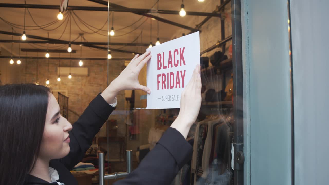 售货员正在她的商店门口贴“黑色星期五”的牌子-慢镜头视频下载