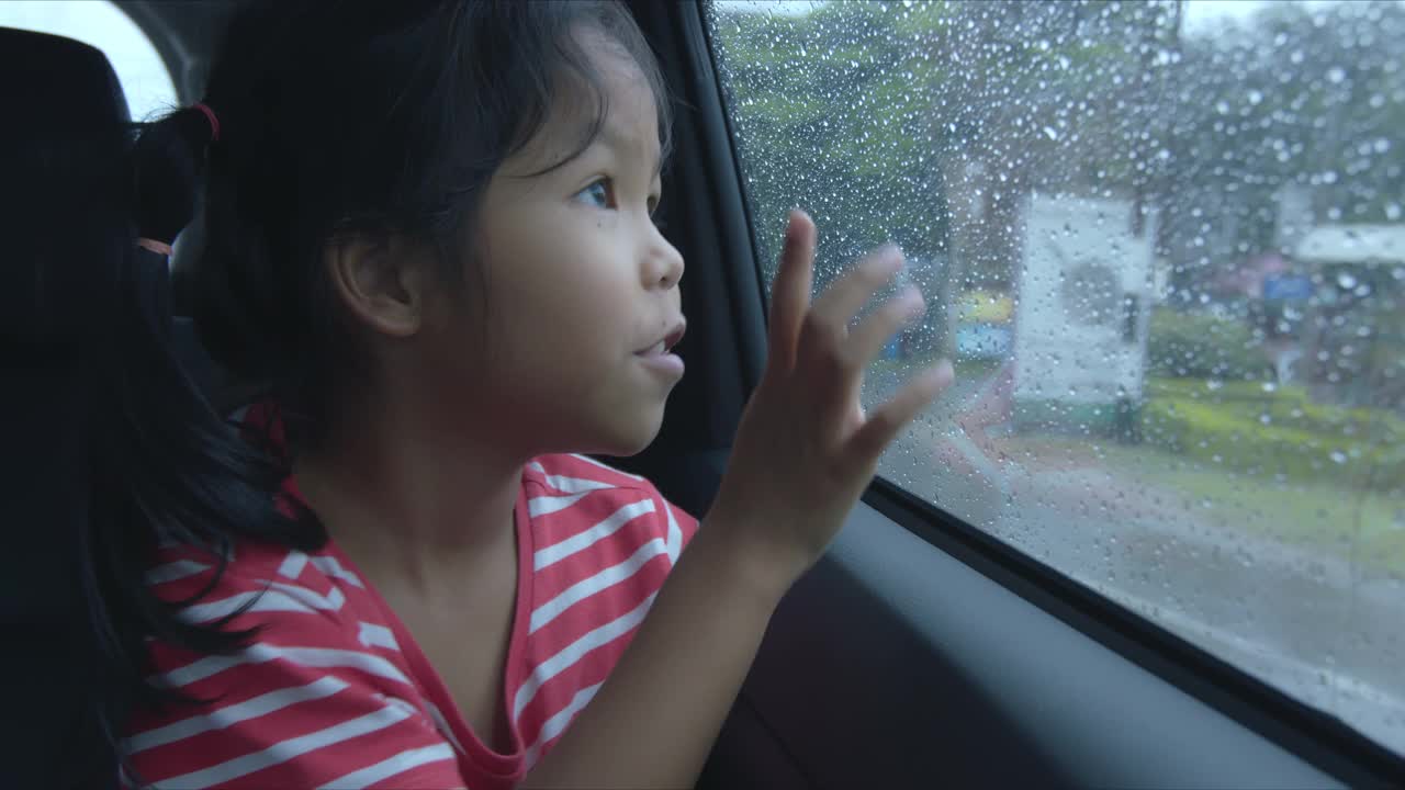 亚洲女孩正在雨天玩汽车玻璃上的水滴视频素材