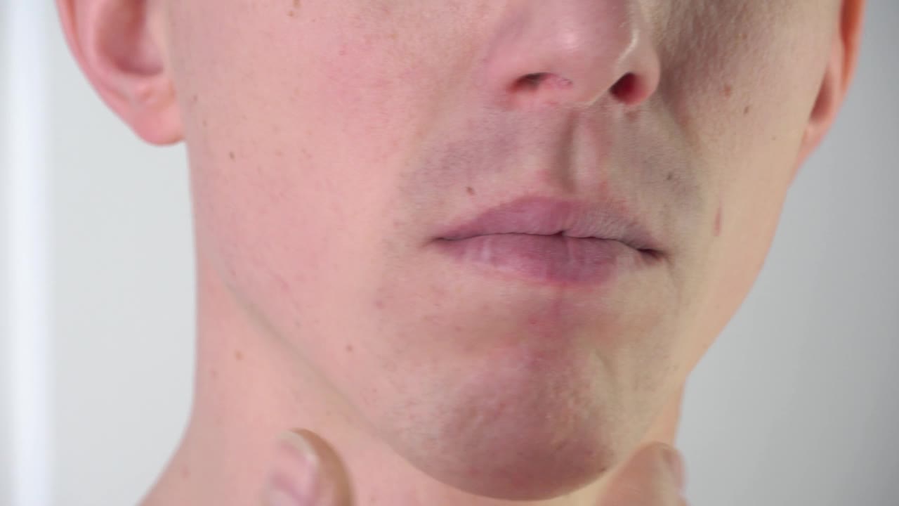在浴室里，一个年轻男子在剃须后抚摸着自己的脸。面部皮肤护理、剃须、胡茬、小胡子和络腮胡。一个剃头的人。皮肤问题、皮疹、黑头、粉刺视频下载
