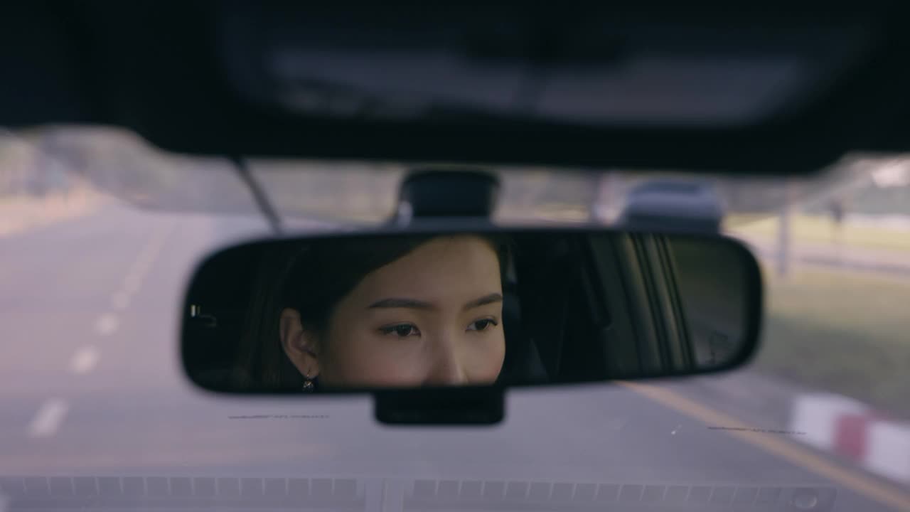 近距离亚洲妇女驾驶汽车反映在后视镜上的道路视频下载