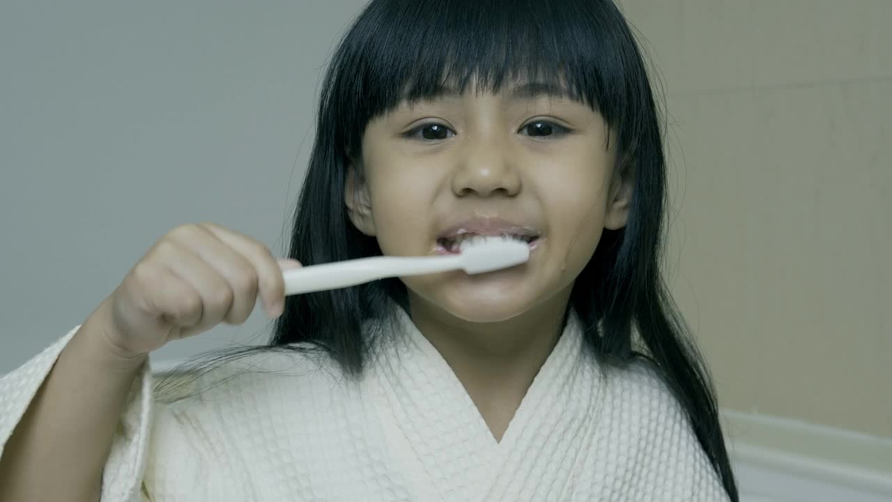 一个亚洲小女孩在浴室里用牙膏勤奋地刷牙。视频下载