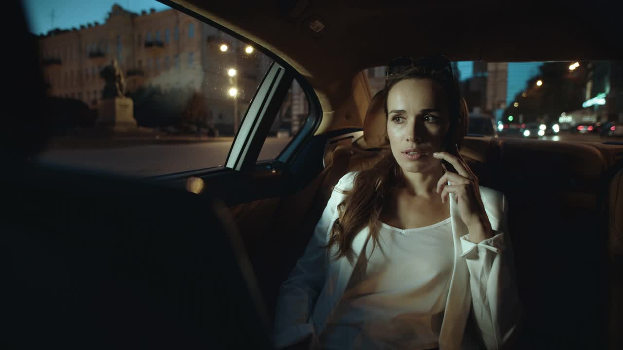 冷静的商务女性在黑暗的沙龙的商务车谈论智能手机。视频下载