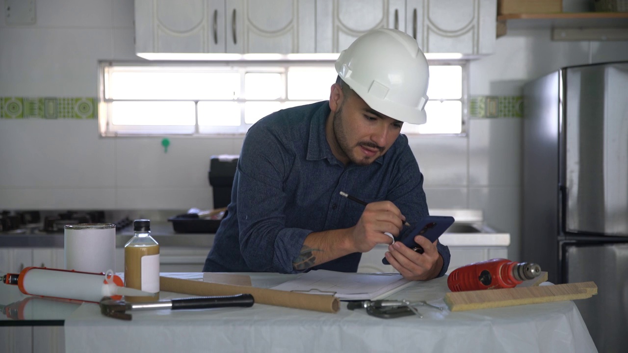 年轻男性建筑工程师在一个家庭装修设计文件，而看智能手机视频素材