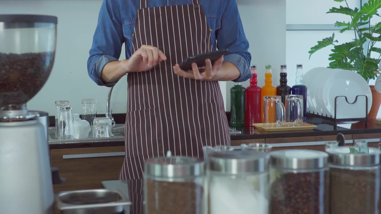 年轻的咖啡师在咖啡店里使用数码平板电脑。视频素材