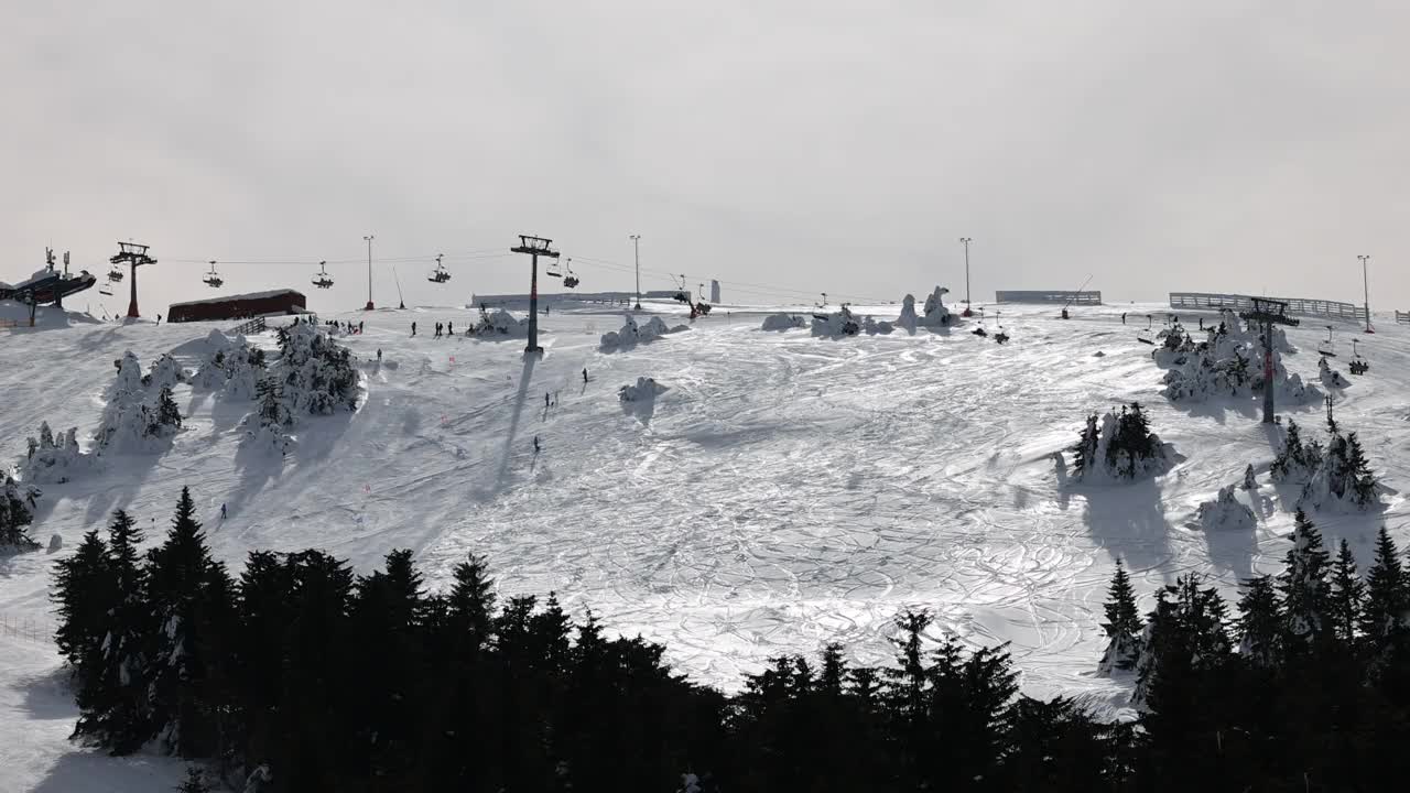 在阴天的冬季，在索道上移动的升降机和在滑雪道上滑雪的滑雪者视频素材