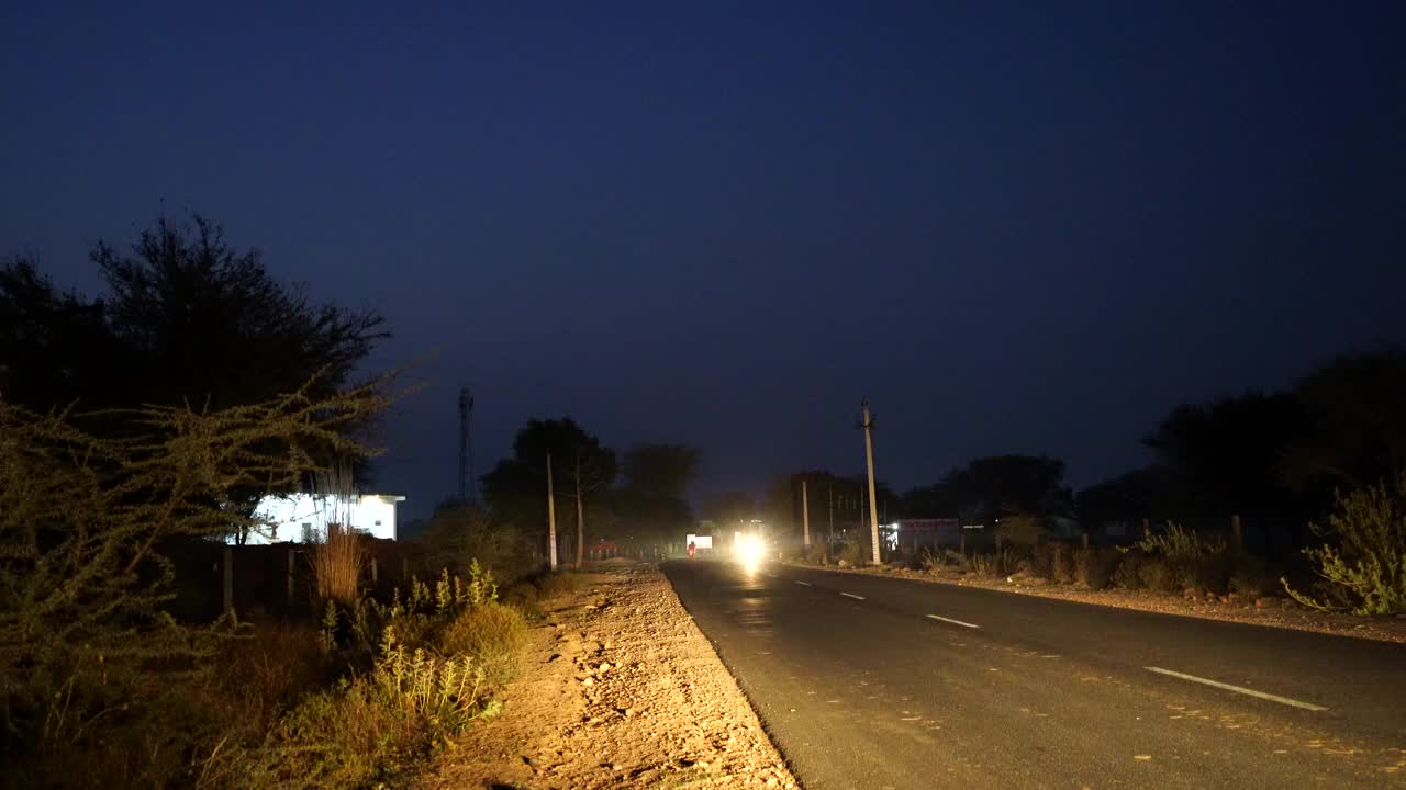 在黑暗的道路上，一辆汽车的前灯向我们驶来。在路上用闪光灯快速行驶的车辆。视频素材