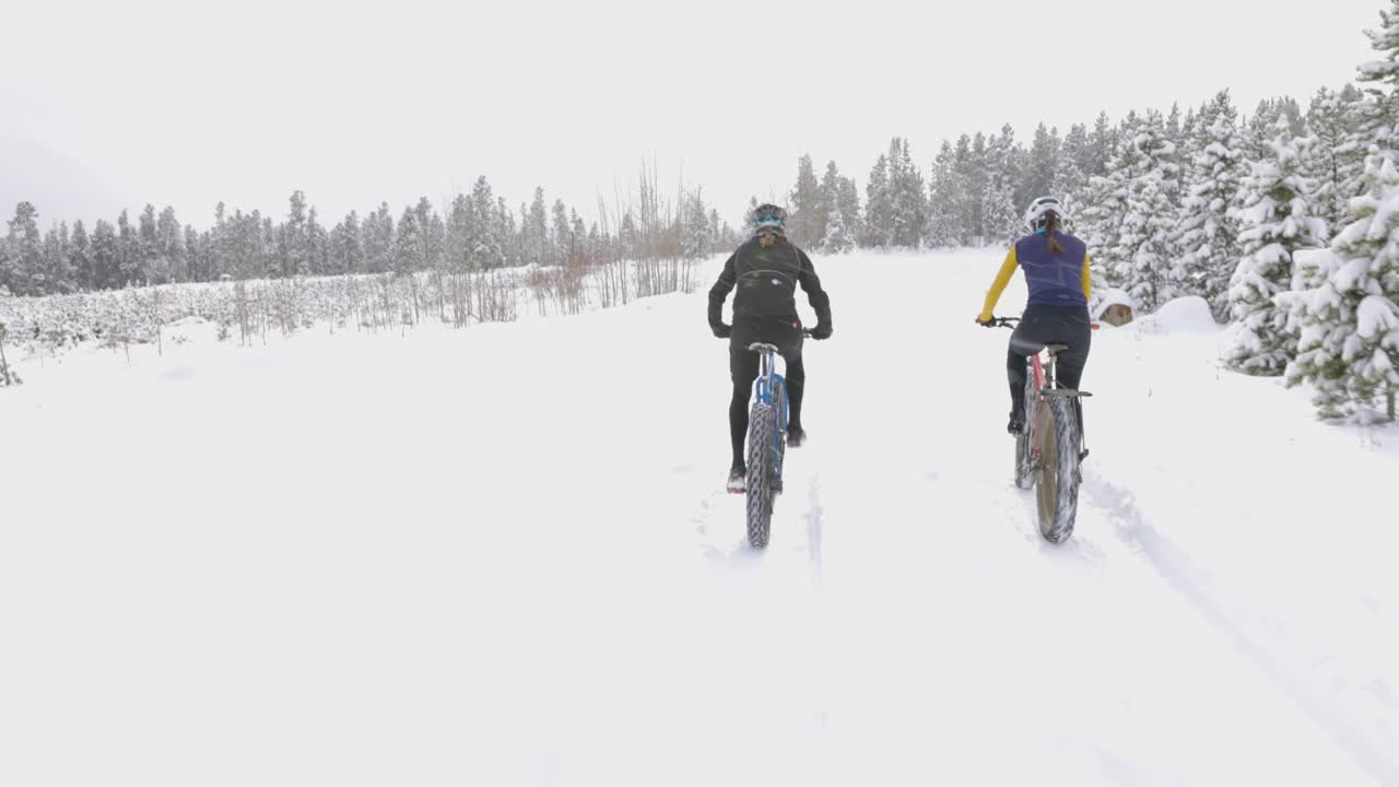 在冬天的下午，女性朋友们在覆盖着积雪的森林道路上骑着胖胖的轮胎自行车视频下载