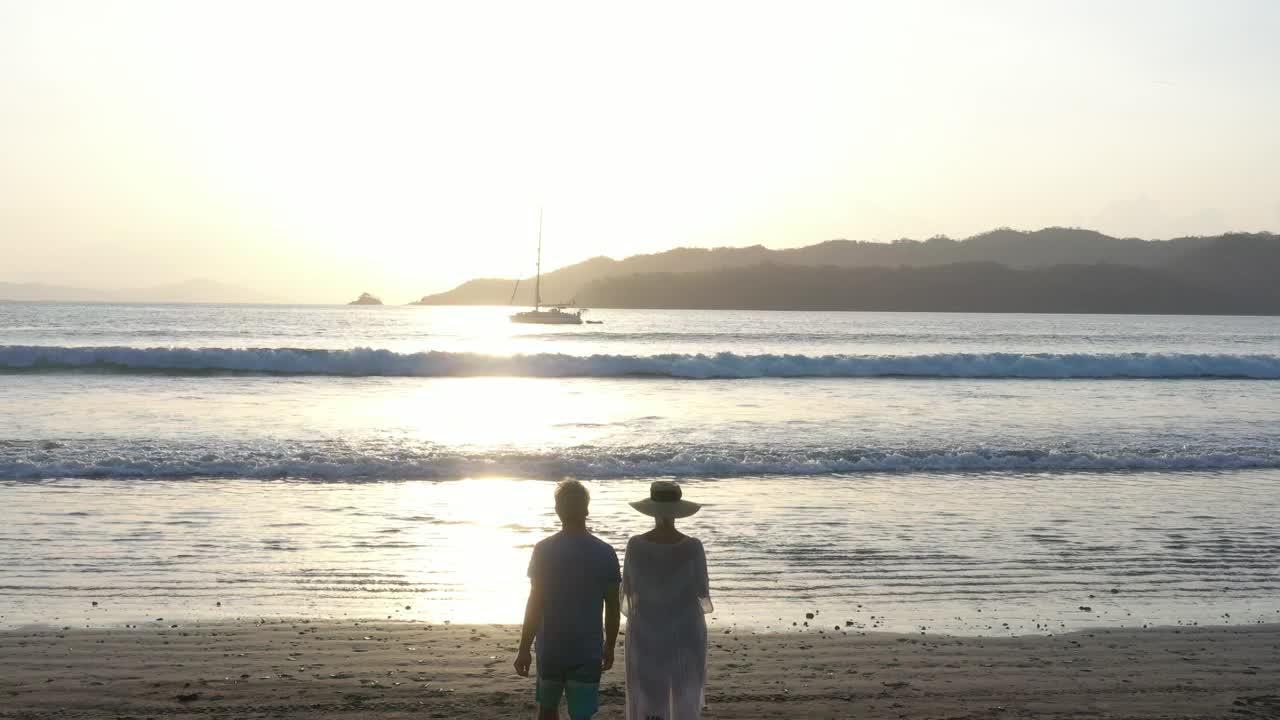 鸟瞰图的成熟夫妇走在空旷的海滩，在日出视频素材