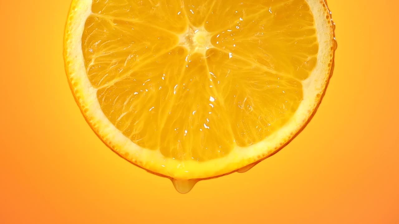 鲜榨橙汁滴从成熟的水果切片近距离橘黄色背景慢动作放大视频素材