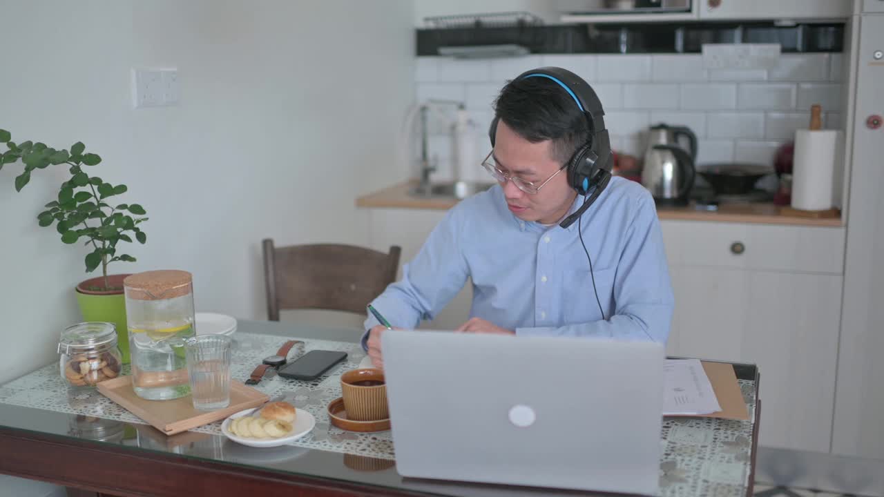 亚洲华人中年男子正在厨房里上网络课，早上还在用笔记本电脑视频素材