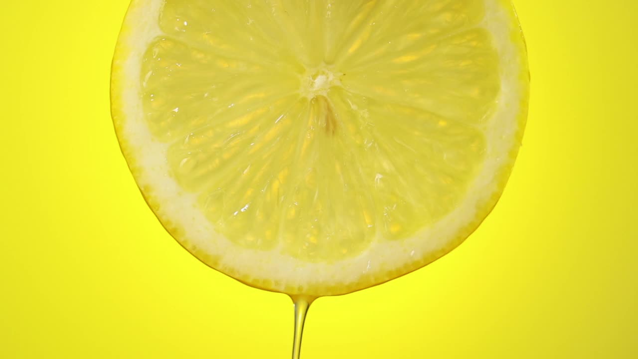 鲜榨柠檬汁流从成熟的水果片近距离在一个黄色的背景视频素材