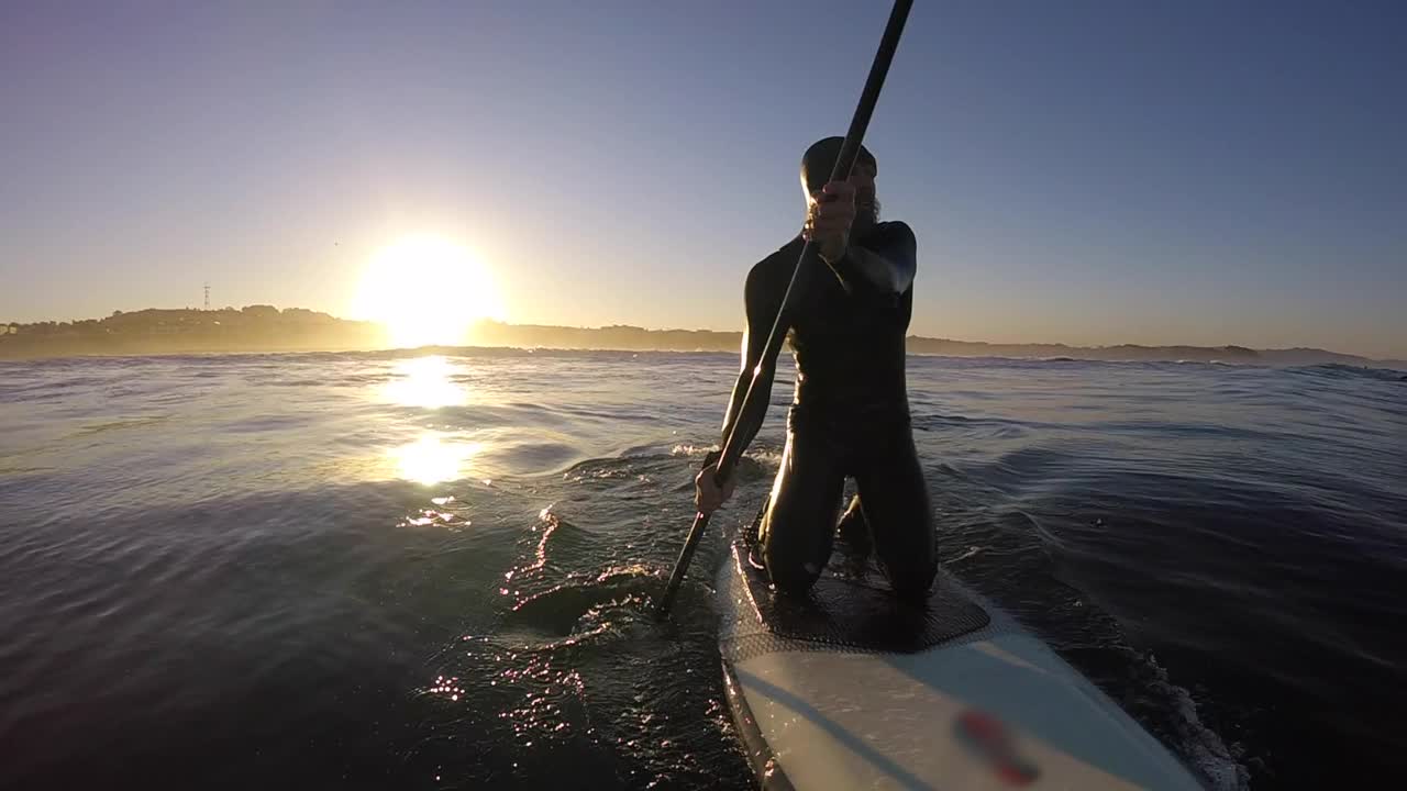 男人跪着，SUP，直立，冲浪板冲浪POV在日出。视频下载