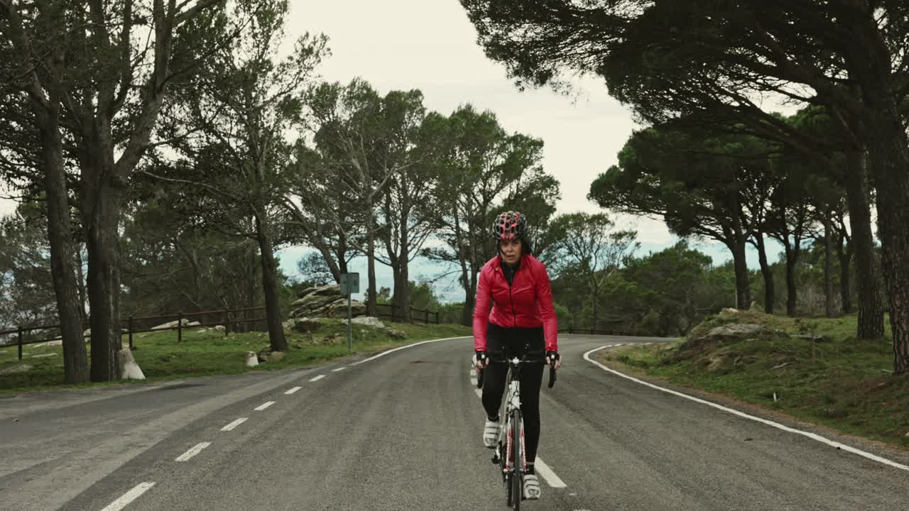 成熟的西班牙女性骑自行车在沿海公路上坡视频素材