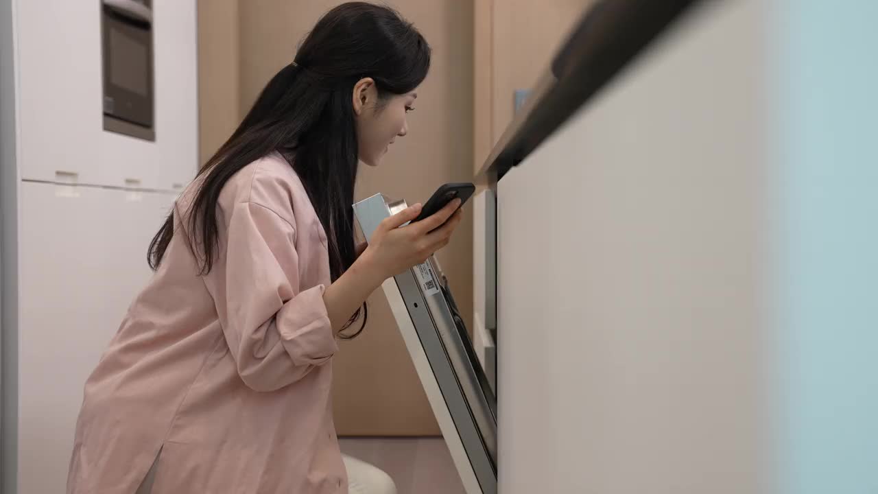智能家居-年轻女子用智能手机检查洗碗机的状况视频素材