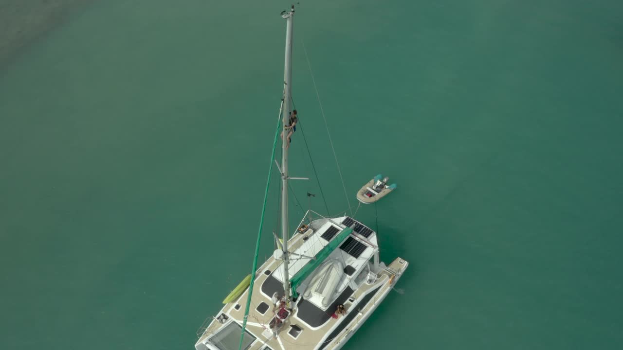 空中盘旋的一个人，当他爬上一艘船的桅杆被蓝绿色的海洋和反射的涟漪阳光-约克角，澳大利亚视频下载