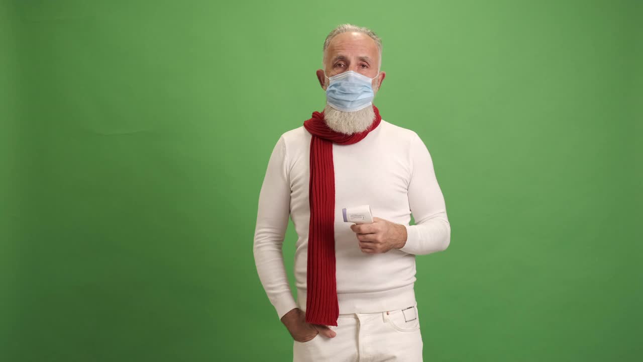 一位戴着医用口罩的老人测量了温度，他很享受看到的结果，并在绿色背景上竖起大拇指视频下载