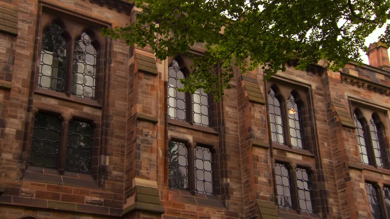 哥特格拉斯哥大学的外墙，有高耸的拱形窗户，支柱，和明亮的灰色天空视频下载