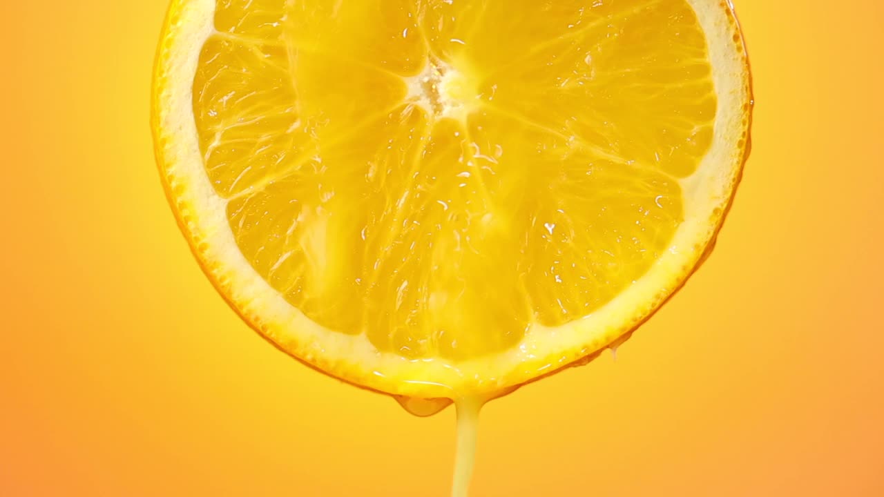 鲜榨橙汁流从成熟的水果片近距离在一个橙色的背景视频素材