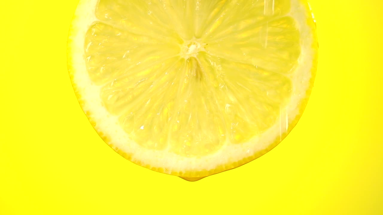鲜榨柠檬汁滴从成熟的水果切片近距离在黄色的背景视频素材