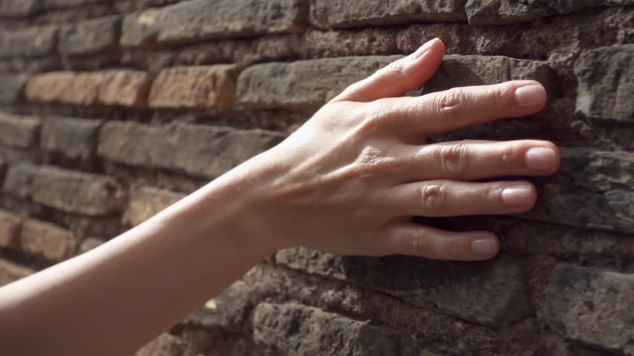 在慢镜头中，一个女人的手靠在古老的红砖墙上。女性的手触摸石头粗糙的表面视频素材