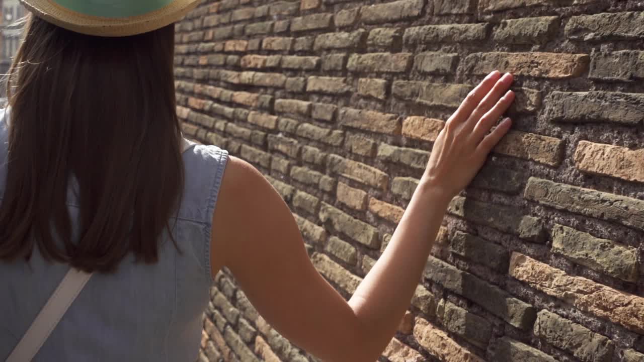 在慢镜头中，一个女人的手靠在古老的红砖墙上。女性的手触摸石头粗糙的表面视频素材