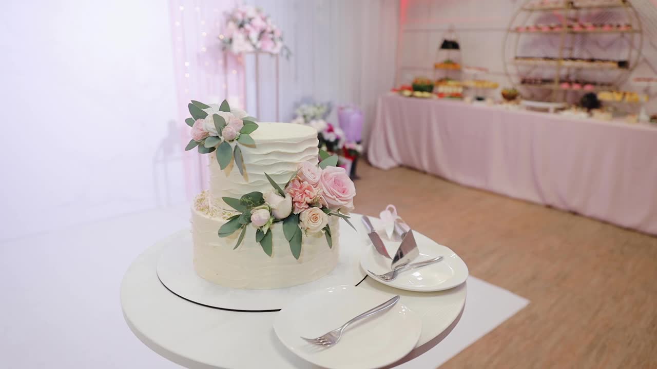 自助餐桌上放着一个美丽、美味的两层白色婚礼蛋糕，上面装饰着鲜艳的粉色玫瑰和绿色的小叶。替身拍摄视频素材