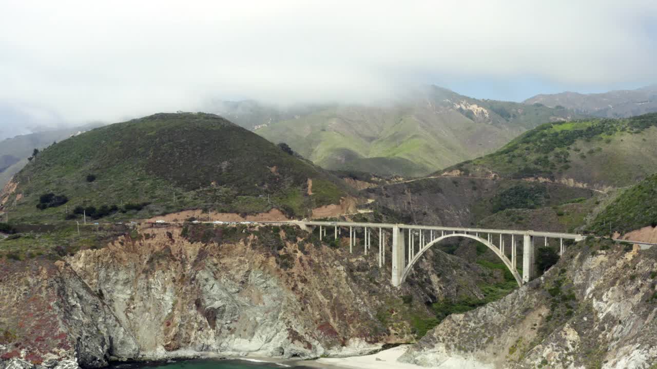 空中移动的高速公路1桥跨越两座山，与云，蓝色的天空，汽车，和滚动的山在背景-大苏尔，加利福尼亚视频下载