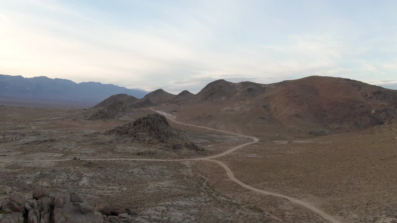 空中拍摄的泥土路在岩石景观对天空，无人机向前飞向汽车吹灰尘在阿拉巴马山-塞拉，加州视频下载