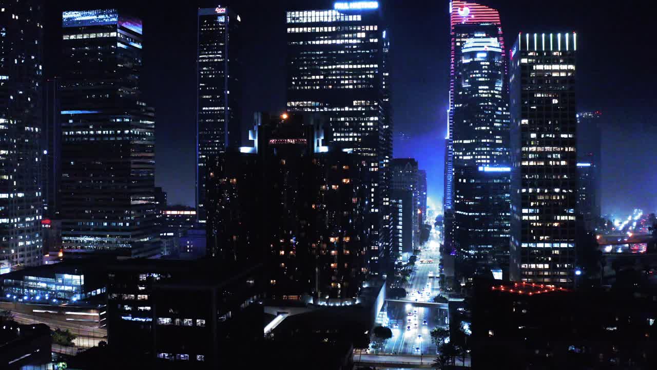 航拍的车辆在街道上照亮摩天大楼，无人机下降在城市的现代高层建筑在夜晚-洛杉矶，加利福尼亚视频素材