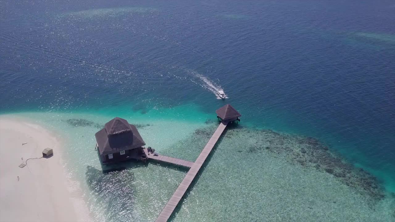 航拍拍摄的摩托艇到达度假码头上的蓝色的海，无人机在晴朗的一天在绿松石水上飞行-瓦杜，马尔代夫视频素材