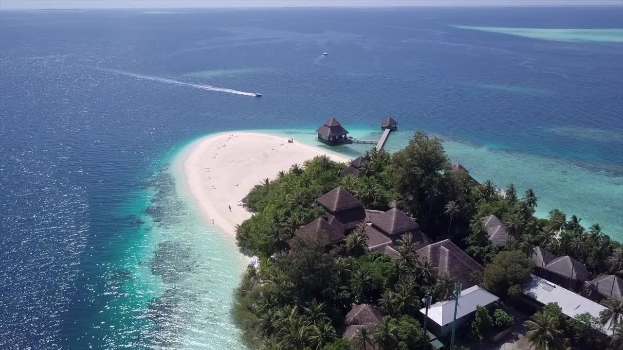 航拍的摩托艇到达度假村码头在蓝色的海，无人机在阳光明媚的一天在海滩上的树木上向前飞行-瓦都，马尔代夫视频素材
