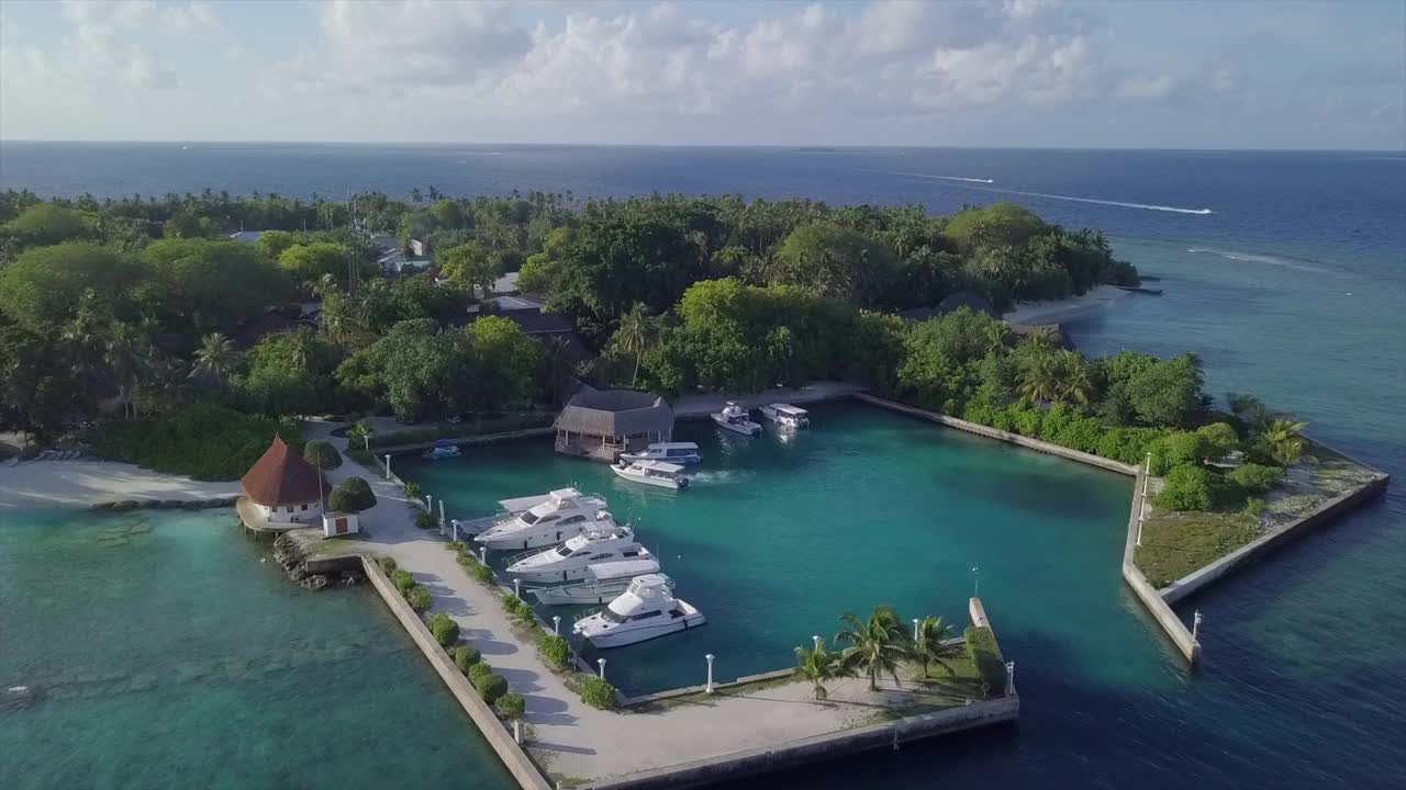 航拍的游艇停泊在港口的树木在岛上，无人机向后飞行在蓝色的海洋对天空-班多斯，马尔代夫视频下载