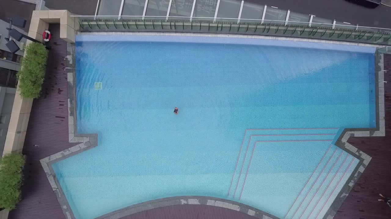 鸟瞰在建筑物中游泳池游泳的人，无人机上升在城市街道上的车辆-香港，中国视频素材