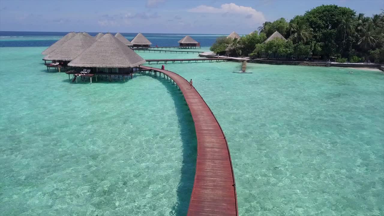 航拍的女人走在码头上的绿松石海，无人机向前在豪华度假村的游客对天空-瓦都，马尔代夫视频下载