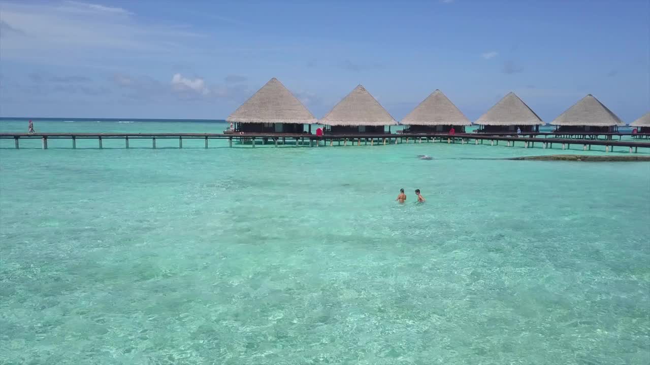 航拍:无人机向前飞过碧绿的海面，游客们在水上小屋附近的天空中游泳——马尔代夫，瓦都视频素材
