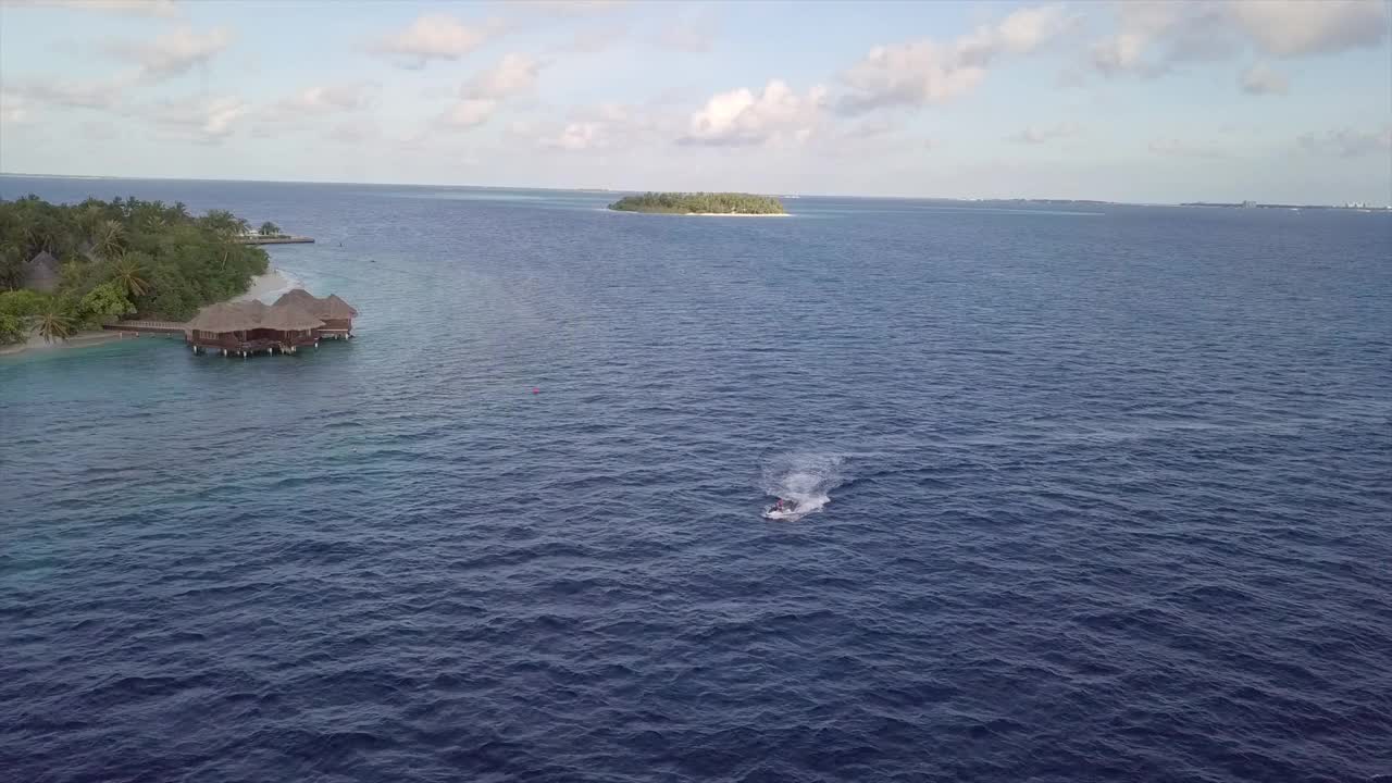 空中倾斜向下拍摄的人在蓝色的海上滑雪对天空，无人机向后飞行在游客享受水上运动-南马累环礁，马尔代夫视频下载