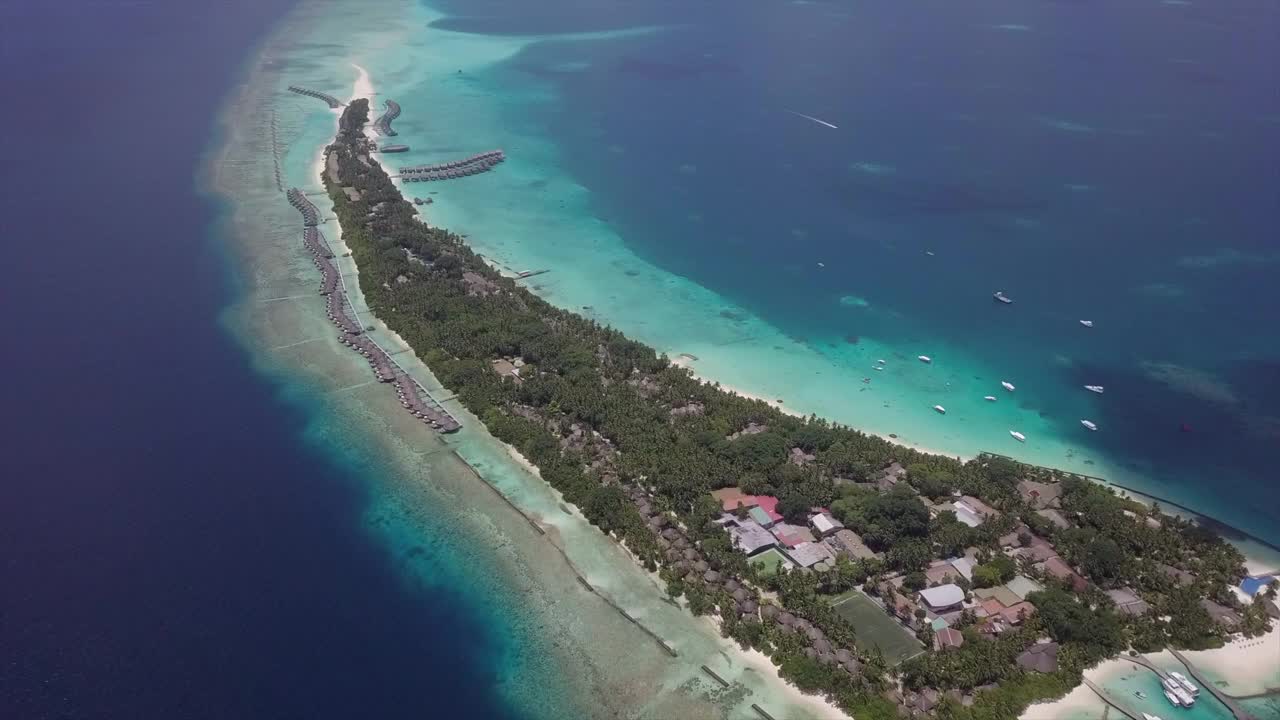 空中向上倾斜拍摄的蓝色海洋周围的岛屿度假胜地在晴朗的一天，无人机向前飞行在水上小屋对天空-南马莱环礁，马尔代夫视频下载