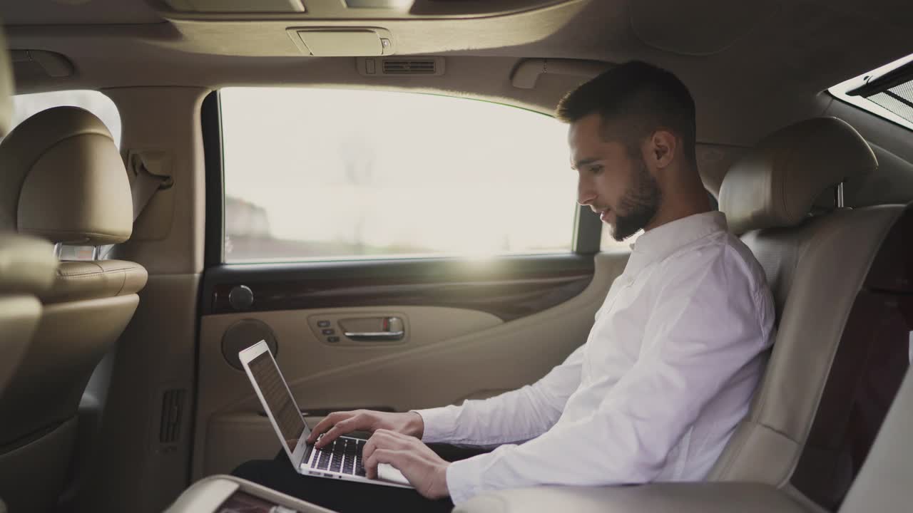 一名男子坐在汽车后座上使用笔记本电脑视频素材
